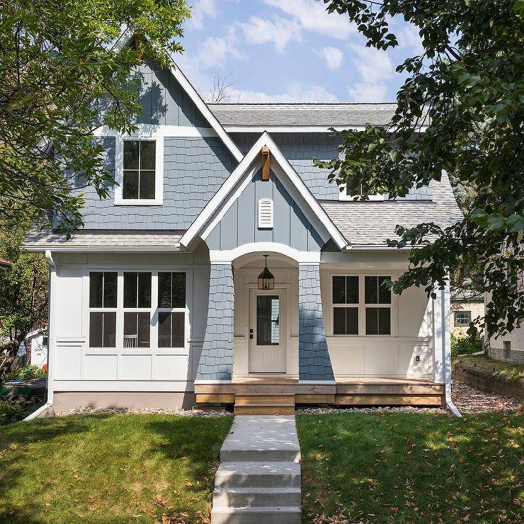 Charming blue bungalow home features concrete steps leading to a blue portico illuminated by an iron lantern hung in front of a glass panel white front door.