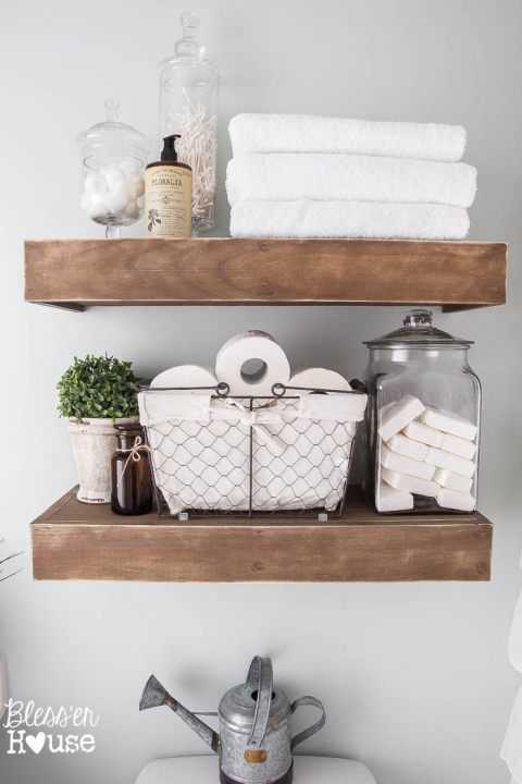 Two thick floating shelves made of wood carrying toiletry, soap, and towels.