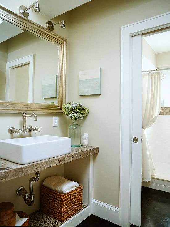 Lovely coastal bathroom design with cafe au lait walls paint color, silver leaf beveled bathroom mirror, brushed nickel bridge wall-mount bathroom faucet, reclaimed wood bathroom vanity shelf, pocket doors and white overmount sink.