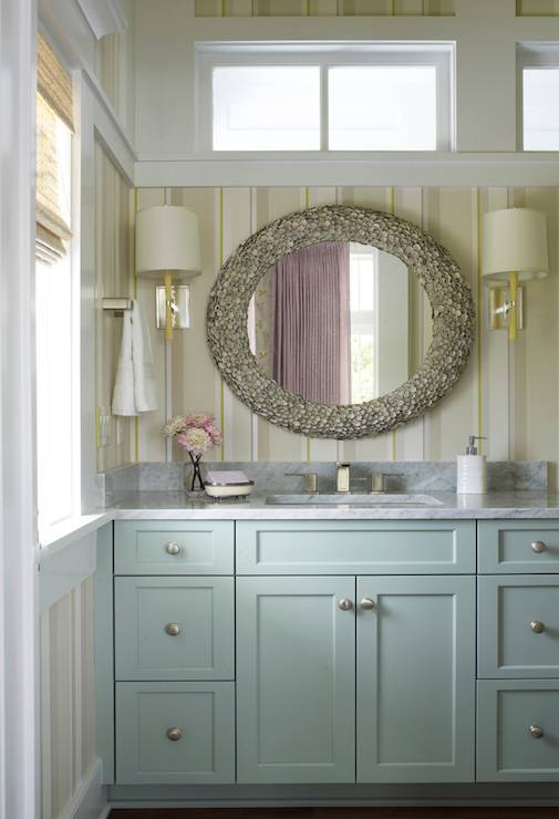 Coastal bathroom features Laura Ashley Eaton Stripe Wallpaper framing Made Goods Jules Mirror flanked by Barbara Barry Refined Rib Sconces over blue vanity painted Sherwin Williams Quietude topped with White Carrera Extra Marble.