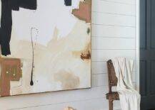 Large abstract art with beige and black tones displayed on shiplap wall. Brown carpet adds to the warm tones complimenting the oversized wall art canvas.
