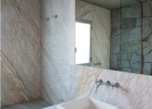 A large bathroom featuring marble walls and a generously sized mirror reflecting the room's ambiance which is mounted above a wood vanity.