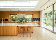 A large open concept med-century kitchen that has a sleek island, modern wood stools, and lots of windows.