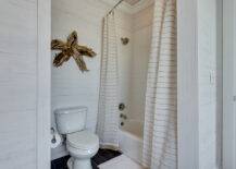 Coastal bathroom features whitewashed oak paneled walls framing driftwood star over toilet next to drop-in tub accented with subway tile shower surround dressed in striped double shower curtains.