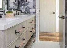 White and gray penny tiles are fixed beneath a gray wash dual washstand boasting a slatted shelf and finished with oil rubbed bronze faucets mounted beneath black Parsons mirrors. The mirrors are lit by white cage sconces mounted against black and white photo collage wallpaper.