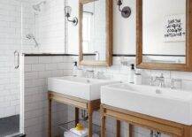 Shared kid's bathroom boasts weathered oak vanity mirror mounted on white walls accented with white subway backsplash tiles positioned behind side-by-side Restoration Hardware Weathered Oak Single Washstands placed on black hex floor tiles lit by industrial cage sconces. The washstands are located next to a subway tile and glass enclosed walk-in shower completed with black hex floor tiles framed by white subway surround tiles fitted with a polished nickel shower kit.