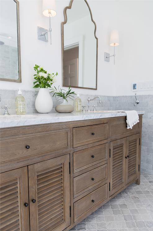 Restoration Hardware Shutter double Vanity features a gray marble countertop and a set of silver arch mirrors above sinks fitted with polished nickel faucets. Gray arabesque floor tiles invite a mosaic finish to the bathroom surface.