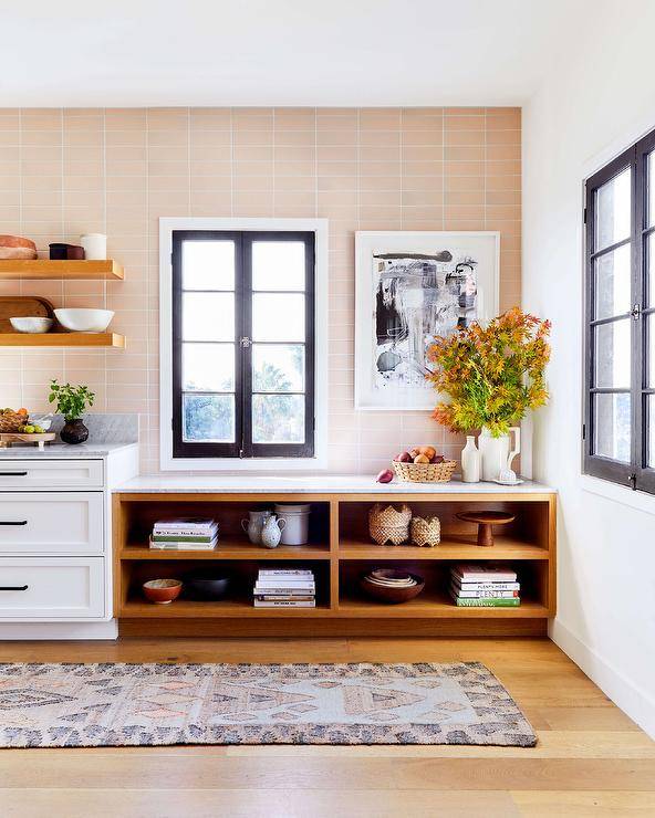 Large kitchen features open shelves fixed against pink backsplash tiles framing a casement window. .