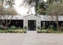 Modern one story farmohouse boasts a gray stone exterior and a plank front door flanked by sidelights.