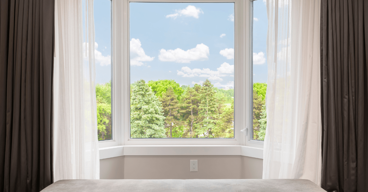 Open bay window curtains with trees outside.