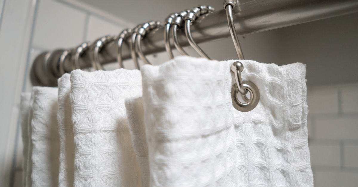 Closeup of fabric shower curtain hung on metal hooks with rollers.