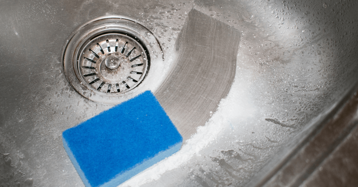 Stainless steel sink with a blue sponge and baking soda inside it.