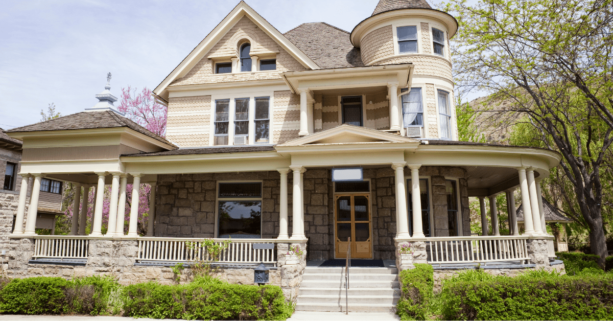 Victorian style house with walk-up stairs and green landscaping surrounding the house.